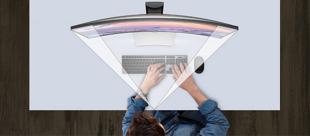 Overhead view of a person typing on a wireless keyboard next to a wireless mouse in front of the curved screen of the Dell UltraSharp U3419W monitor