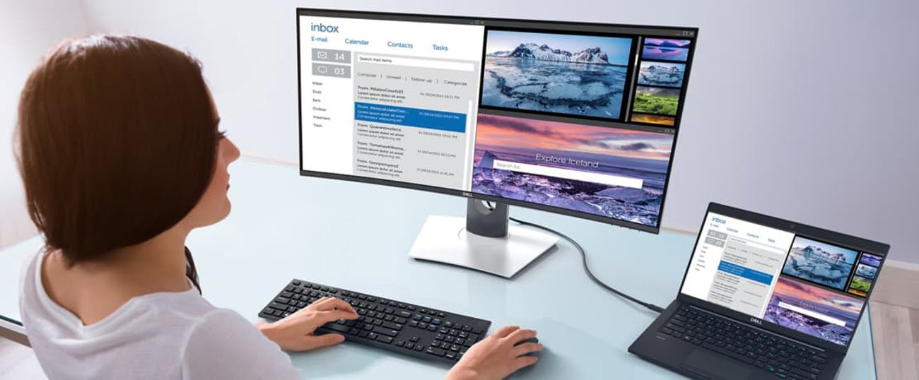A woman at her workstation using a wireless keyboard and mouse next to her open laptop that's plugged into the Dell UltraSharp U3419W Monitor