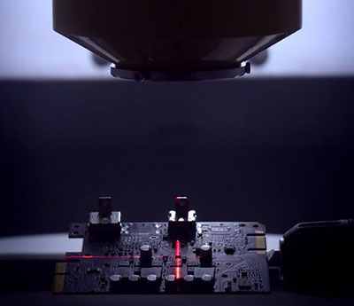 A graphics card PCB below some equipment, with red cross lines on the PCB