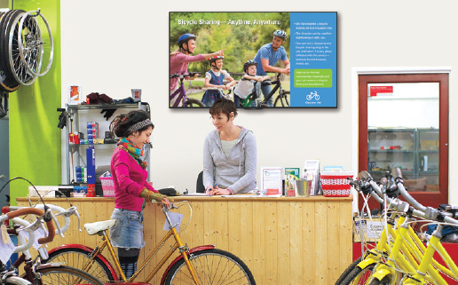 Sharp display mounted over a bike shop's kiosk where two women are in the middle of a transaction