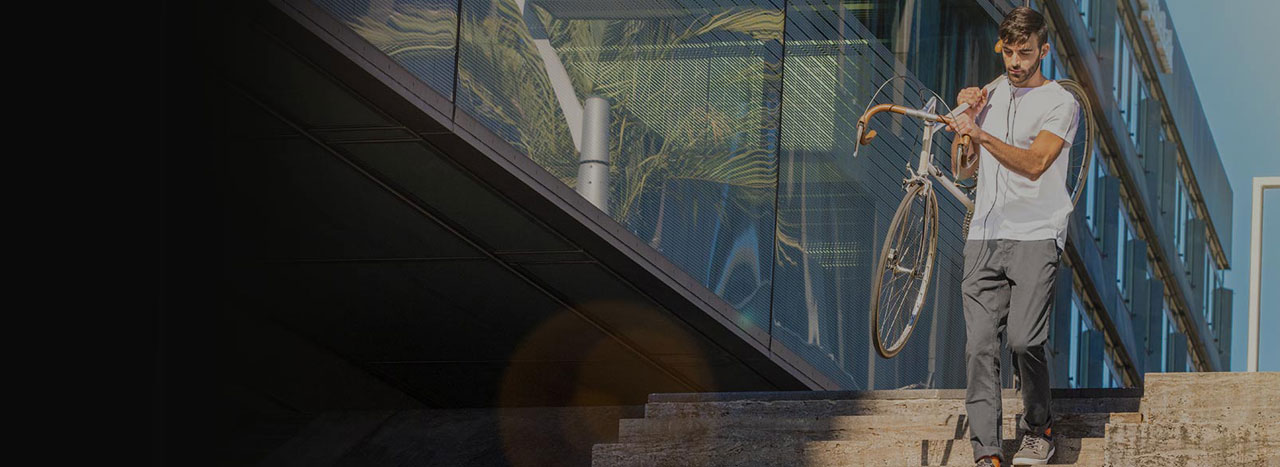 A man carrying his bike down a flight of stairs next to a glass-covered building
