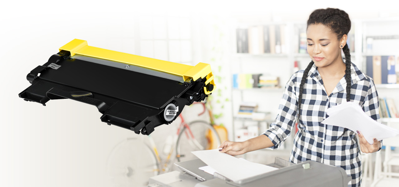 Rosewill RTCA-TN450-2PK toner cartridge at the forefront of a background image of a woman taking paper from a printer in a home-office setting