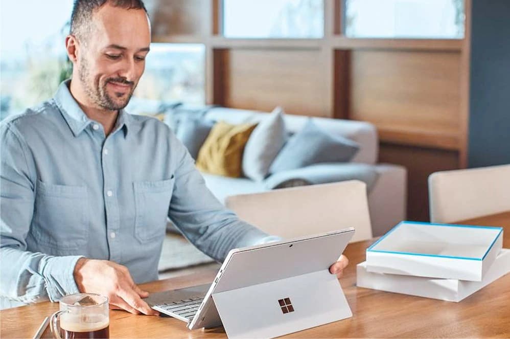 a man happily using his Surface Pro placed on a wooden desk