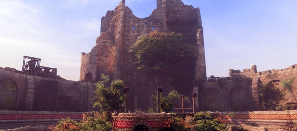 A Plague Tale - Innocence Screenshot Showing a Castle Town Ruined Brick Building in a Town Square