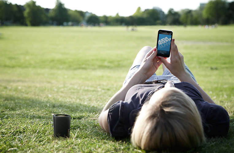 a man laying on the grass is enjoying music from Philips BT100B