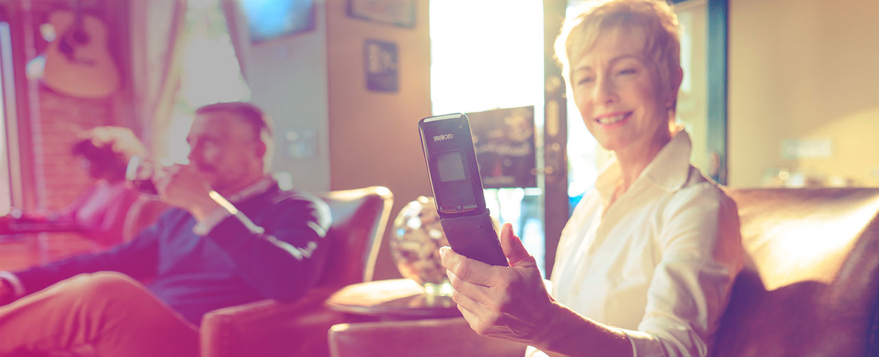 An older man and woman lounging in their living room. The woman is smiling looking at her open Alcatel A405 phone