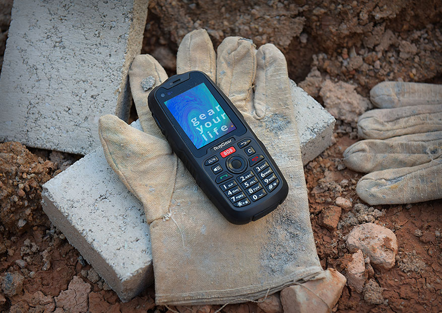 RugGear RG310 Phone lying down a work glove on a brick in dirt