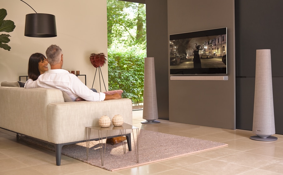 A man and woman on a couch in their modern-home living room watching TV with the citation towers on the floor on each side of the TV