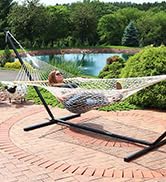 White cotton rope hammock with female model laying outside on a brick pation with lush landscaping
