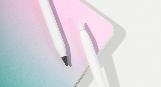 Close-up of white stylus or digital pen resting on pastel pink and teal surface, casting a shadow. Pen tip visible against contrasting background.