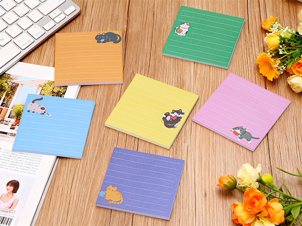 Collection of pastel-colored greeting cards or note cards arranged on wooden surface, featuring various designs and patterns. Flowers visible in corner of composition.