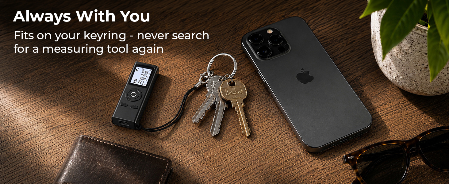 Mini laser measuring tool on a keyring with keys, phone, and wallet on a wood desk