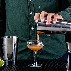 cocktail being poured into a coupe glass from a Boston shaker tin