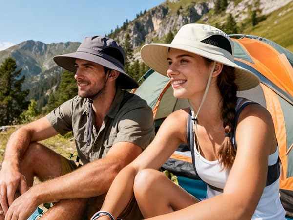 Handsome man & long-haired woman in sun hats by a tent in mountain meadow. For outdoor camping.