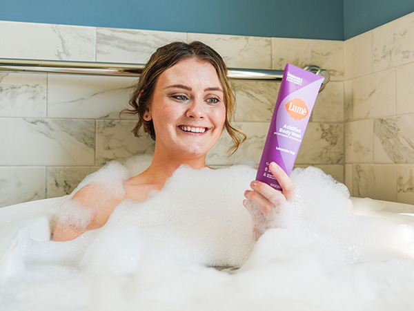 A woman using Lume Acidified Body Wash in Lavender Sage being used in a bath tub