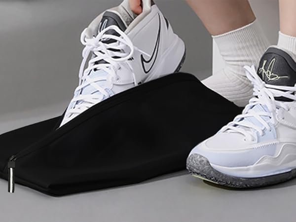 White Nike basketball shoes with gray soles worn on feet. One foot rests on a black mat or surface, demonstrating the shoe's flexibility and fit.