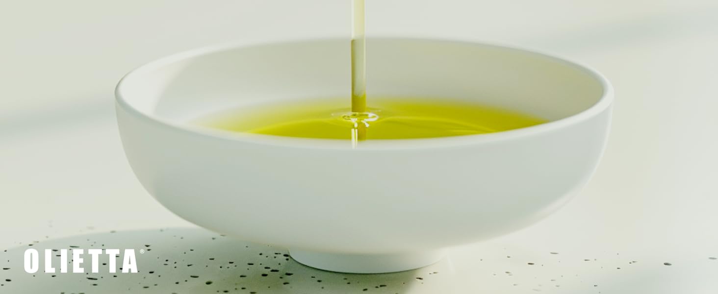 White ceramic bowl with golden olive oil being poured into it, creating a smooth, glossy surface against a light background.