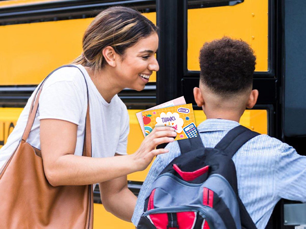 A boy is giving her teacher a teacher note cards to make her feel appreciated.