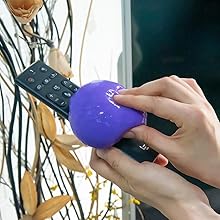 Hands holding a purple, round object and a black remote control near a window with plants visible in the background.