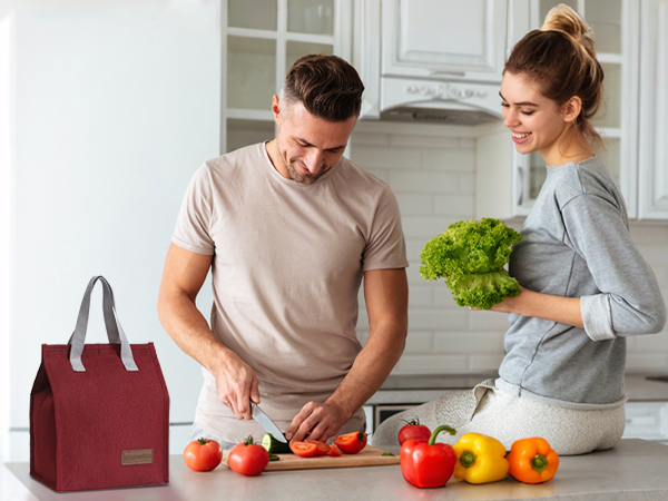 Kitchen scene showing couple preparing fresh produce with burgundy tote bag visible on counter.