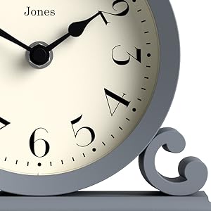 Jones wall clock detail showing elegant black numerals and hands against cream-colored face, with decorative grey scroll detail.