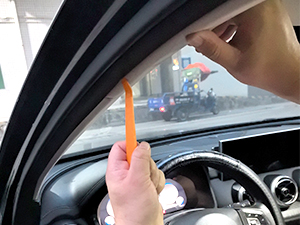 Hand holding an orange plastic automotive trim removal tool inside a car, demonstrating its use near the dashboard.