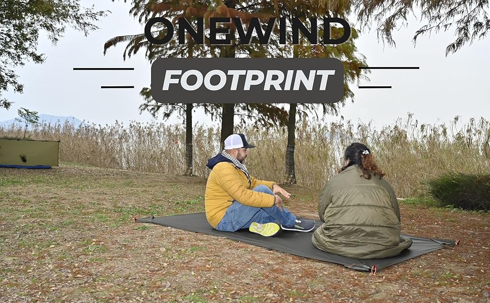 Outdoor scene with two people sitting on a blanket under a sign reading 'FOOTPRINT' surrounded by trees and grass.