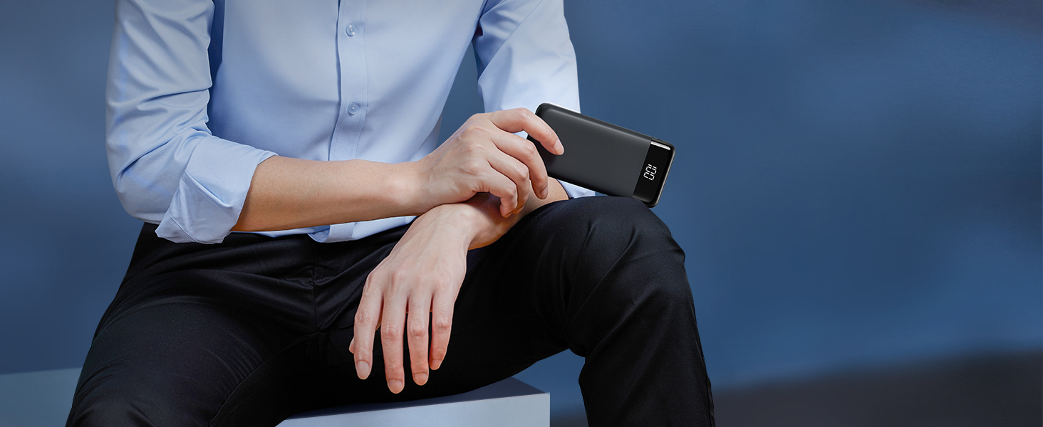 Person in blue shirt sitting, holding smartphone horizontally with both hands. Only torso and hands visible against blue background.