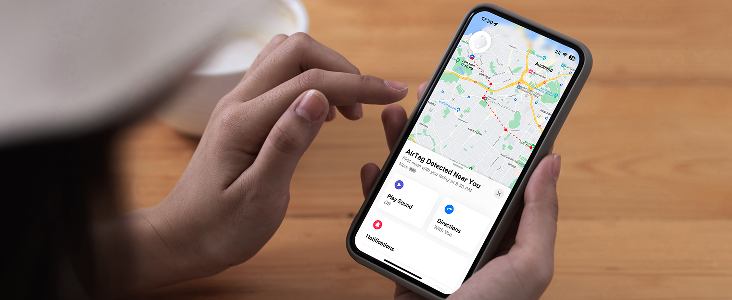Hands holding smartphone displaying pet location tracking app interface with map navigation on wooden surface.
