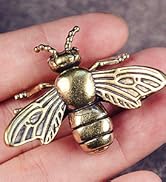 Metallic bee-shaped brooch or pin held in a person's hand. Detailed wings and body with an antique gold finish.