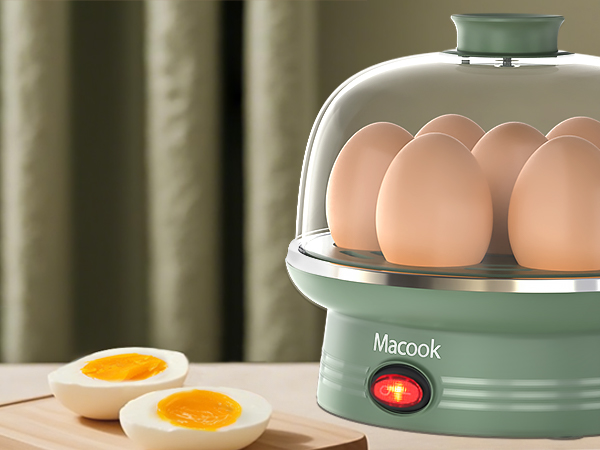 Macook egg cooker with mint green base and clear dome lid. Contains multiple eggs. Boiled egg halves shown in foreground. Red power indicator light visible.