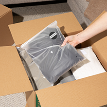A shirt in a frosted bag with a branded circle label being placed in an open shipping box