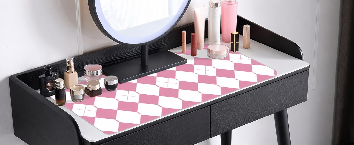 Beauty and cosmetic products arranged on a black organizer tray with pink checkered mat, displayed on table near mirror for makeup application and storage organization.
