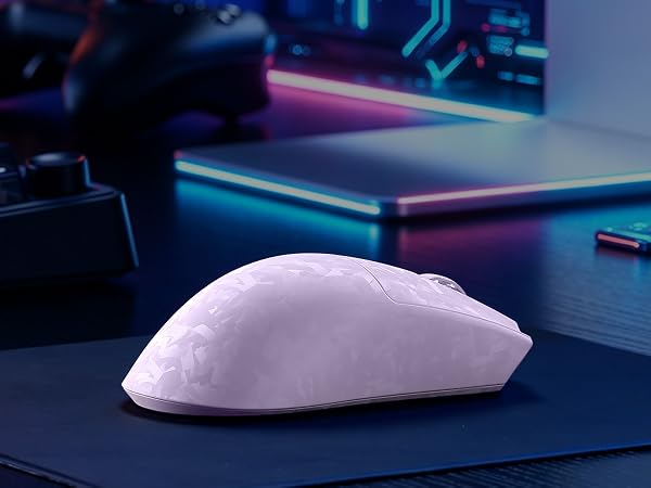 White computer mouse with ergonomic curved design on dark desk surface with neon-lit keyboard and desk accessories visible in background.
