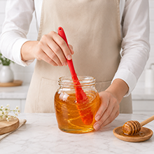 red silicone scraper stirring honey in jar