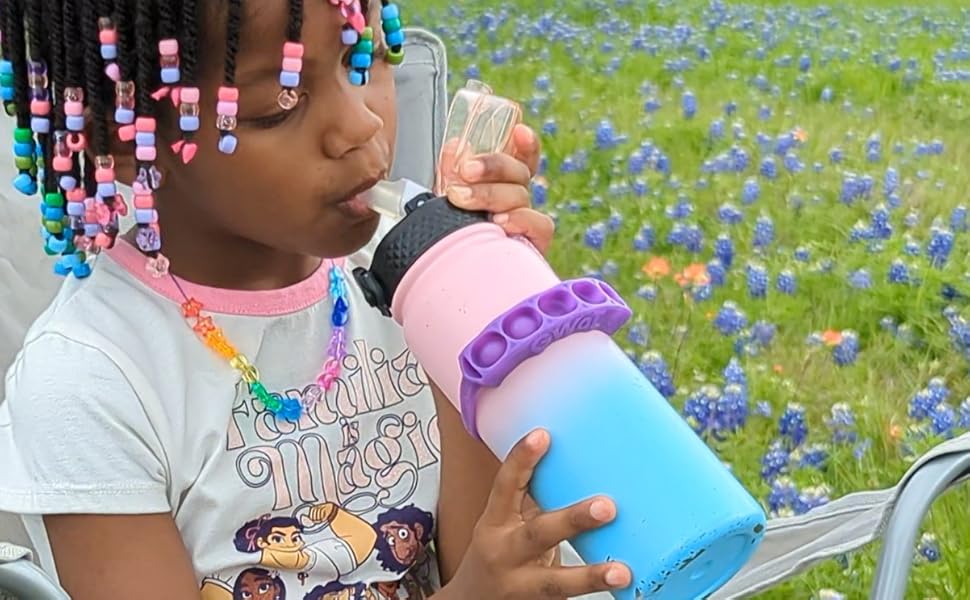 Child sitting in flower field drinking from bottle with GWaT attached.