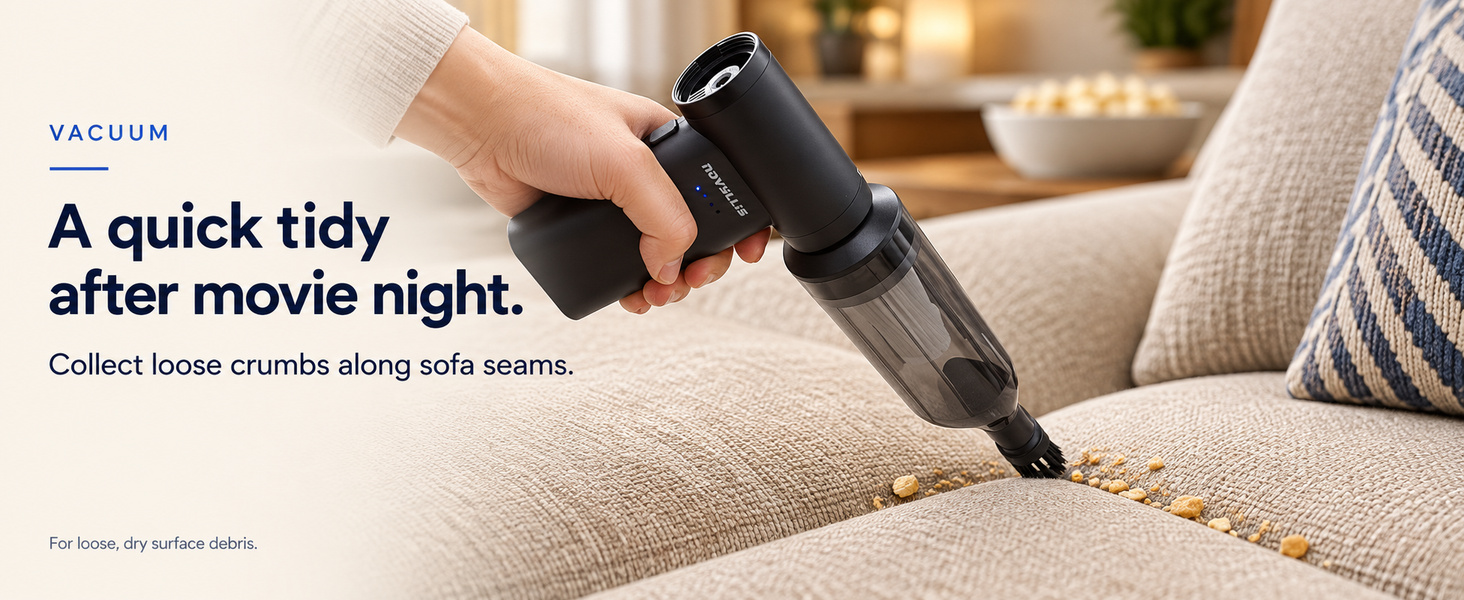 Handheld mini vacuum with brush attachment picking up loose crumbs along sofa seams