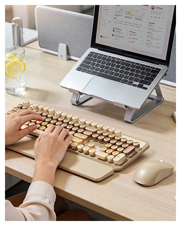 Hands typing on a beige typewriter-style keyboard with matching mouse beside a laptop on a desk.