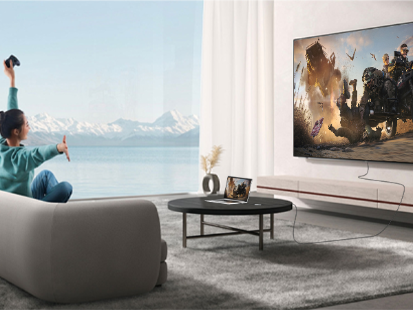 Modern living room setup featuring large wall-mounted TV, grey sofa, and round coffee table, with panoramic mountain view through window.