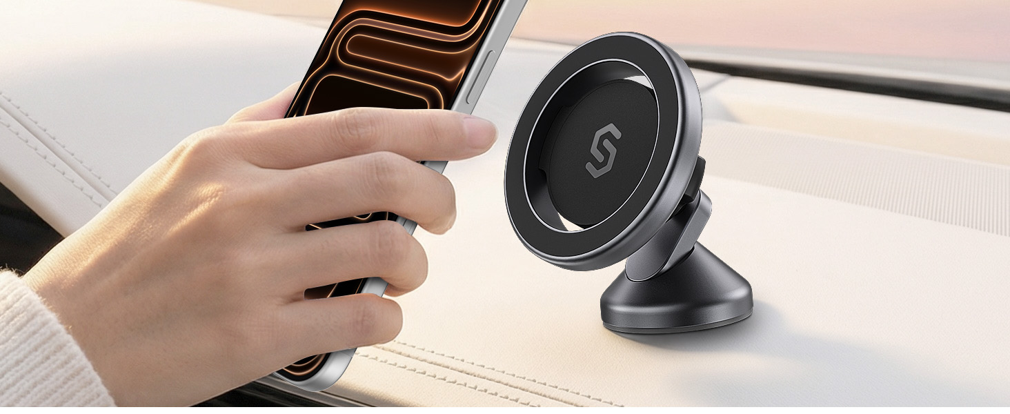 Hand holding circular magnetic smartphone car mount with rotating ball joint, mounted on vehicle dashboard with dark textured surface.