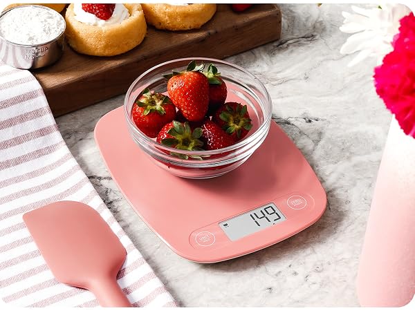 greater goods coral pink kitchen scale on marble counter weighing bowl of strawberries