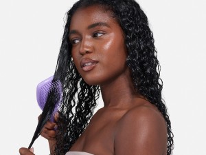 A woman brushing her curly hair with a purple ultimate detangler brush.