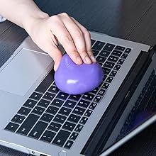 Hand using a purple, egg-shaped object on a laptop keyboard, possibly a cleaning tool or ergonomic device.