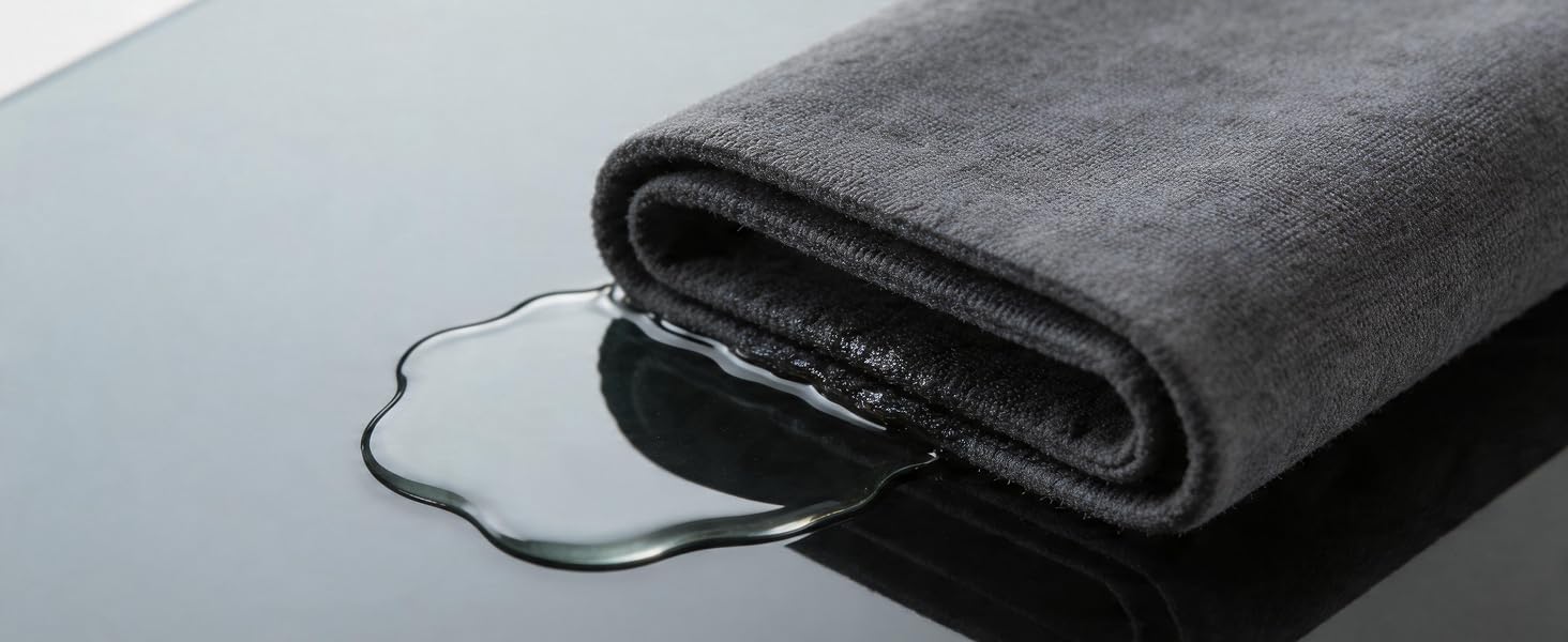 Grey microfiber cloth absorbing water on black glass surface.