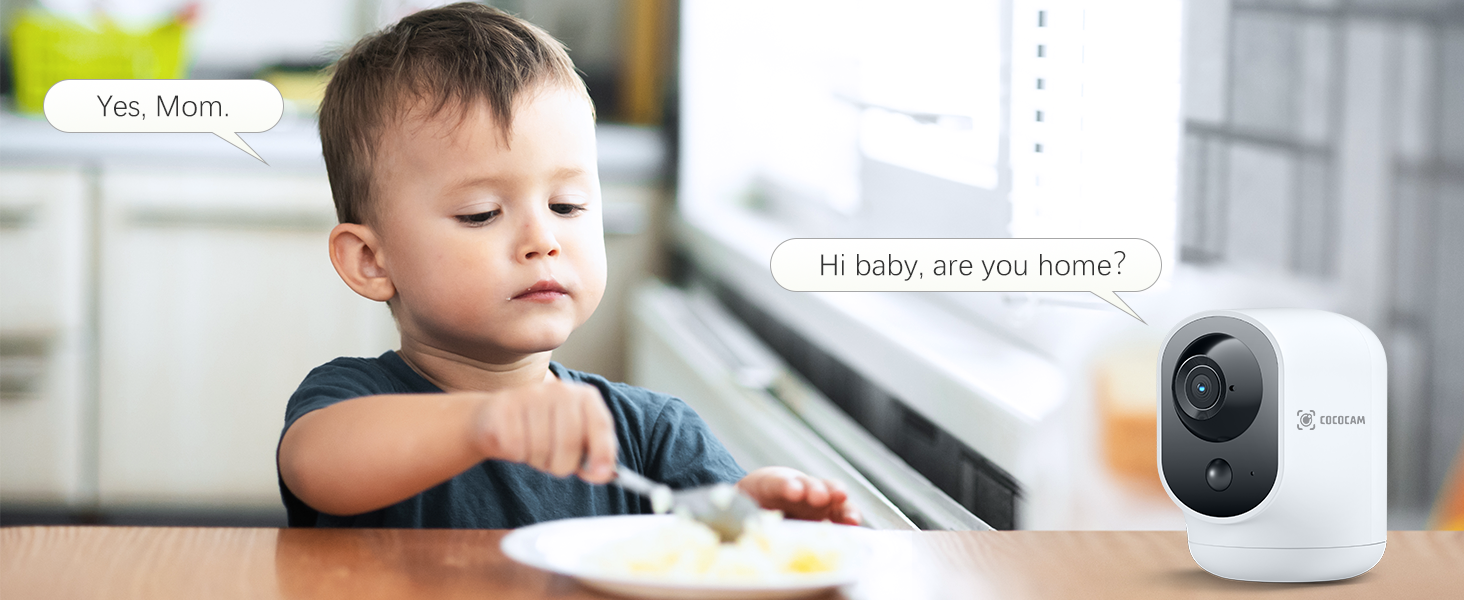 Wireless home security camera on table, with child in background eating at counter. Camera features rounded design with dark lens.