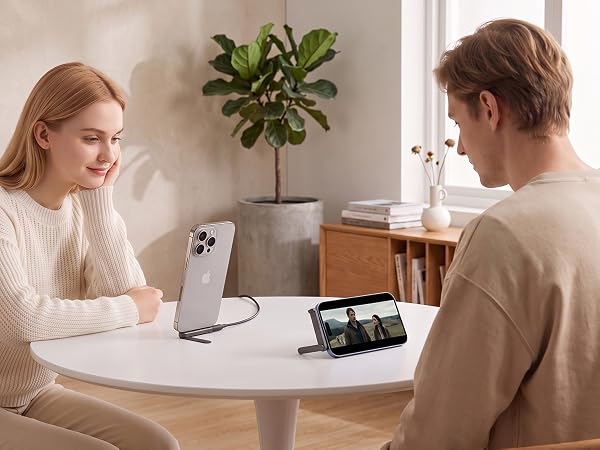 Two people sitting at white table facing each other with laptop and digital devices, discussing or collaborating in bright interior space.
