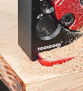 Close-up of a black kitchen appliance with red accents, labeled 'TOOLGOOL', sitting on a wooden surface with sawdust around it.