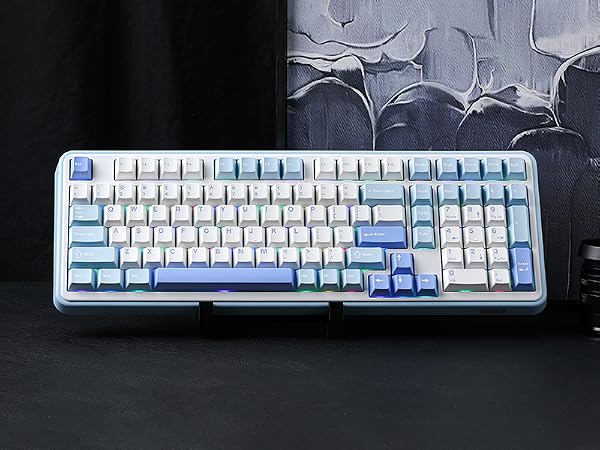 Full-size mechanical keyboard with white and blue keycaps. Features a standard QWERTY layout, numeric keypad, and function keys. Displayed on a dark surface against an abstract background.