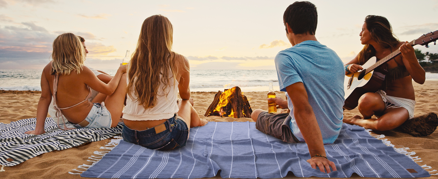 WOMEN AND MEN ARE SITTING ON THE GOLD CASE TURKISH TOWELS AT THE BEACH