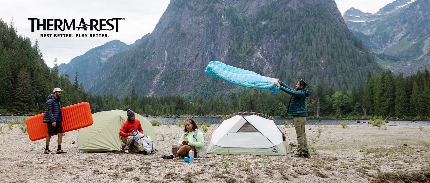 Two people laying in sleeping bags outdoors looking at a map